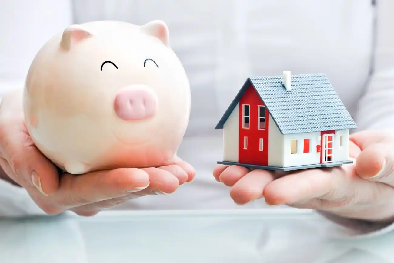 Person Holding a Piggy Bank and Tiny Home