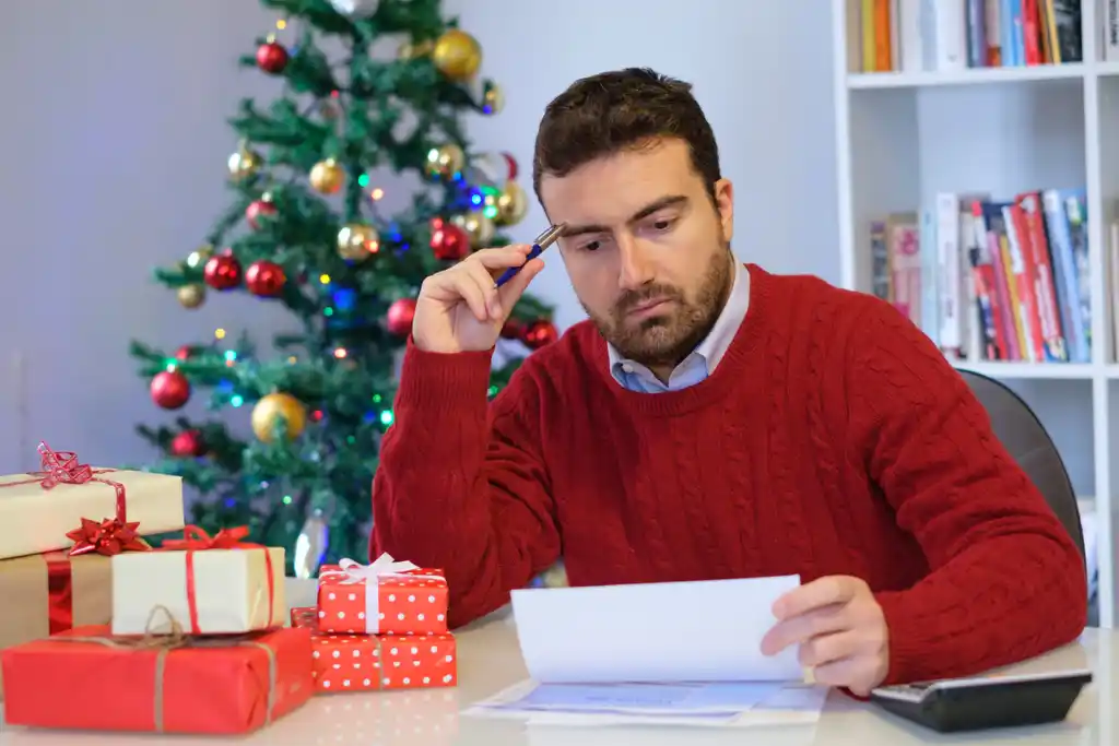 Man Upset Looking at Bills with Christmas Tree