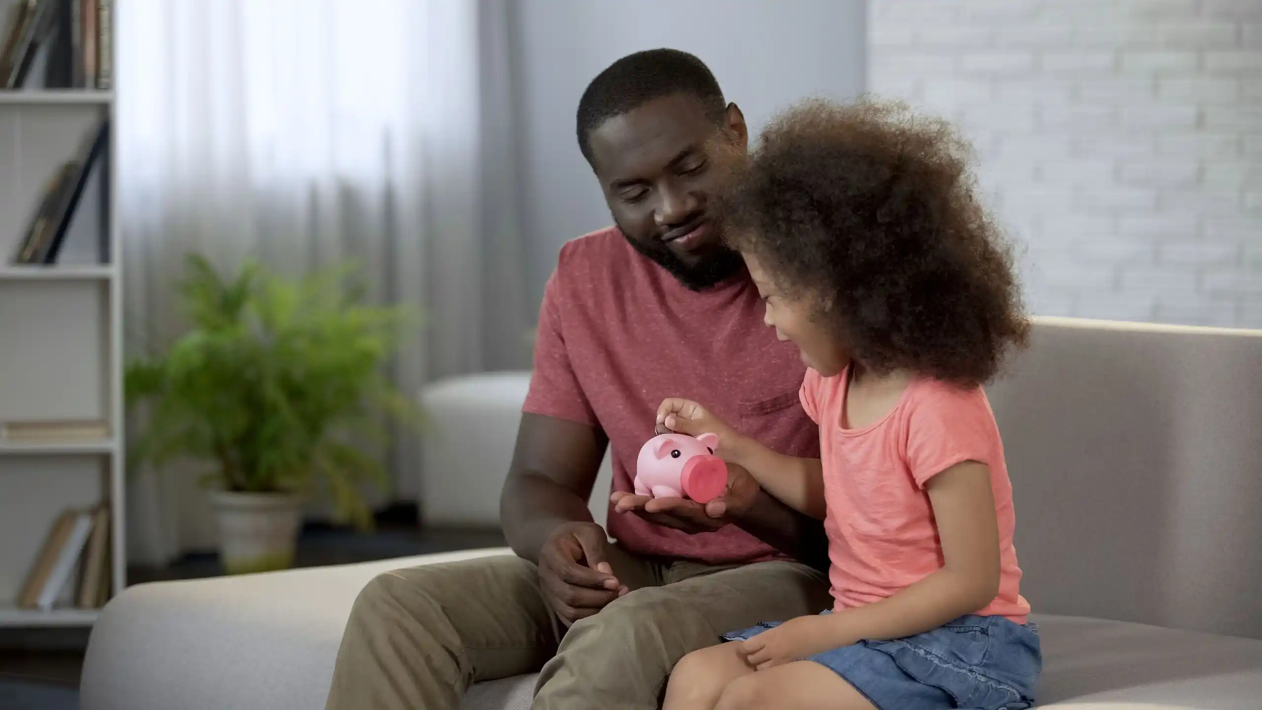 Child Putting Money into Piggy Bank Father is Holding