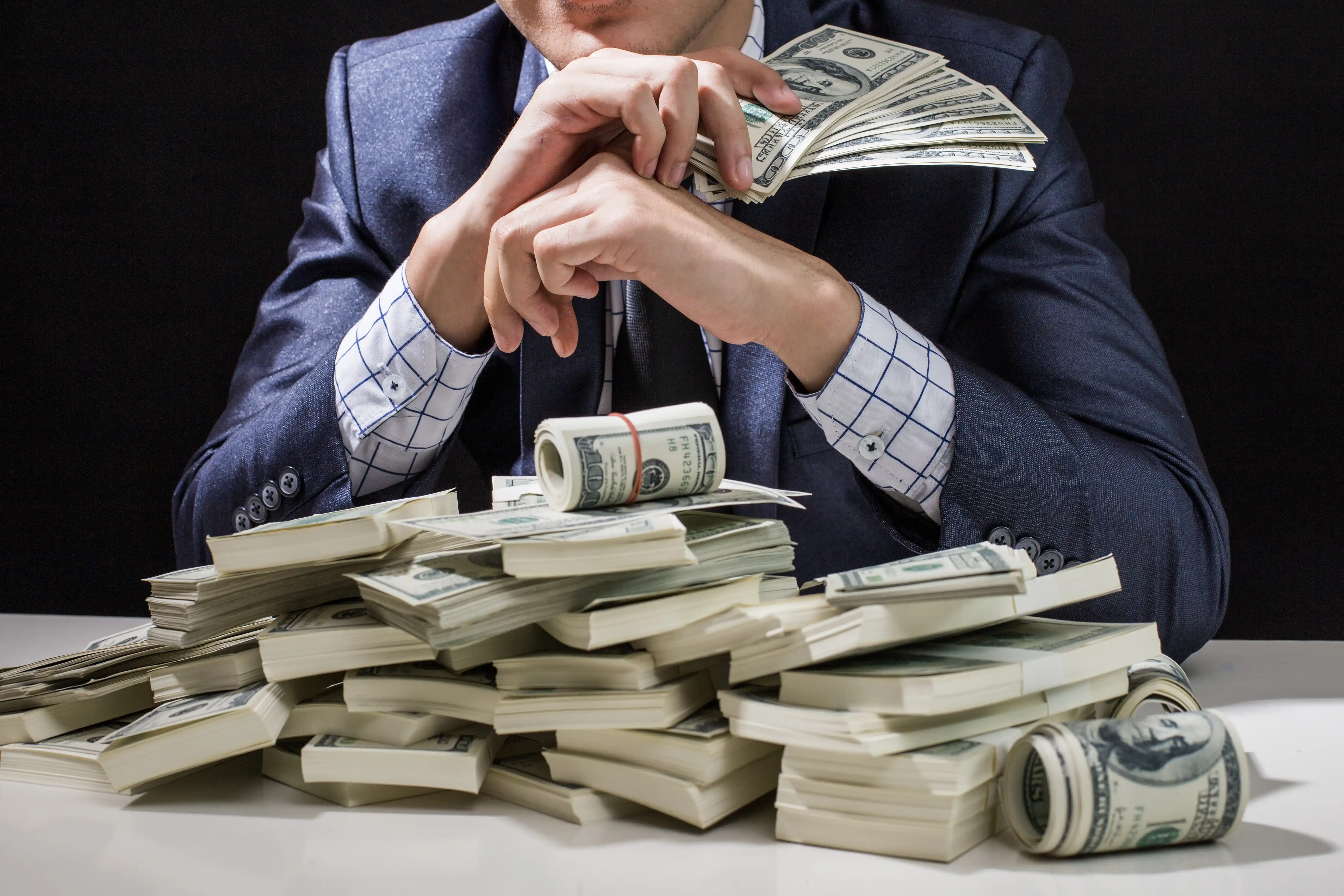 Man in suit sitting in front of pile of cash